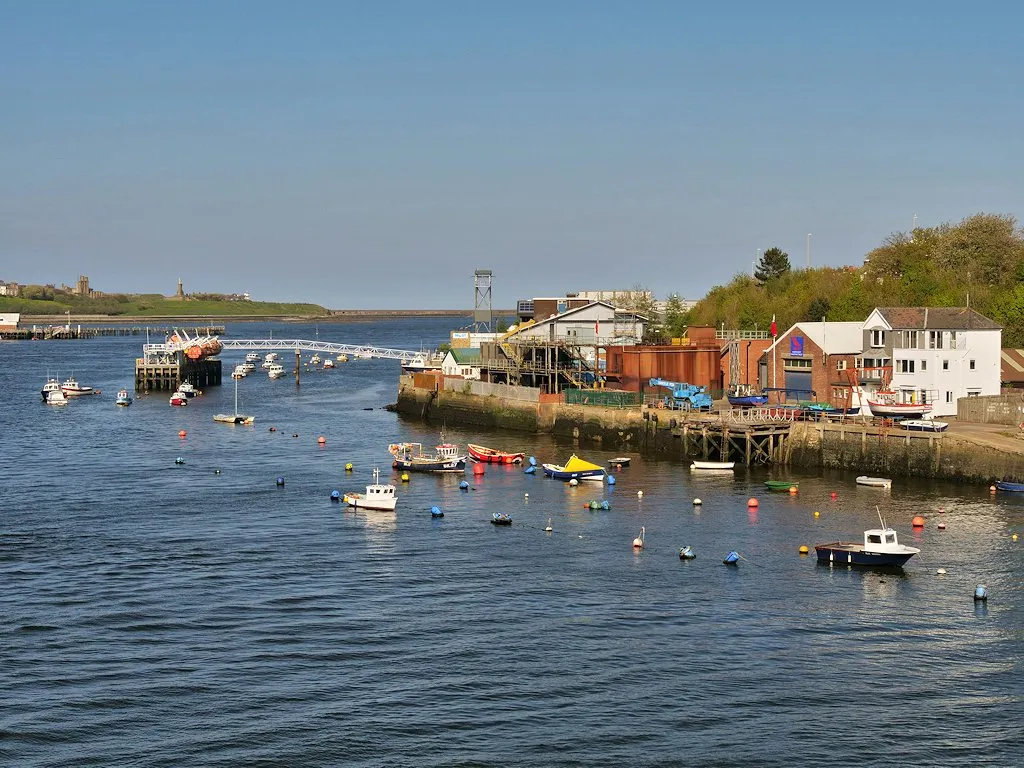 A harbour with small boats on moorings, a pontoon with training equipment and a red-brick building on the waterfront under a blue sky.