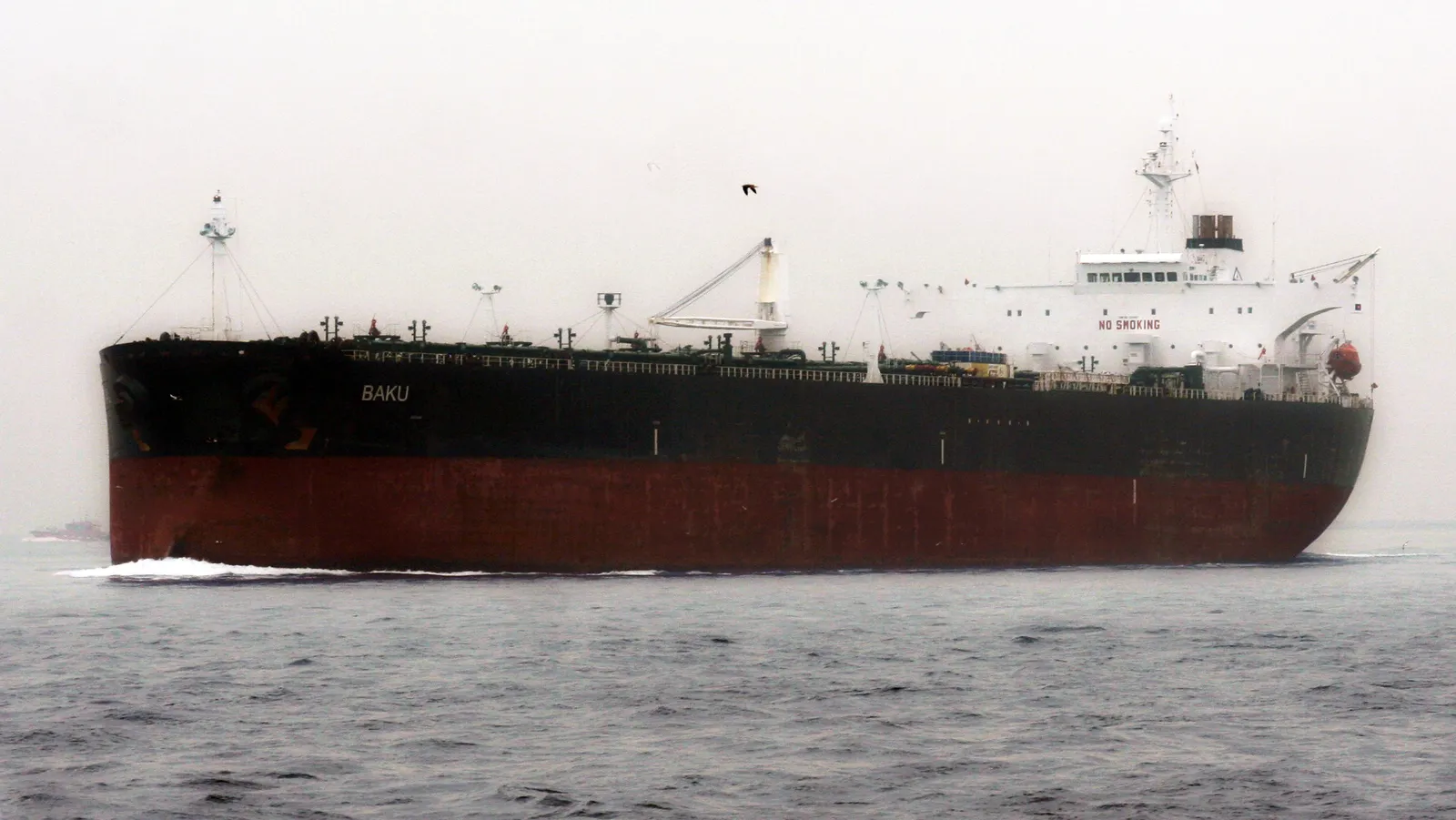 A large tanker with a black and red hull sails through grey water on a misty day.