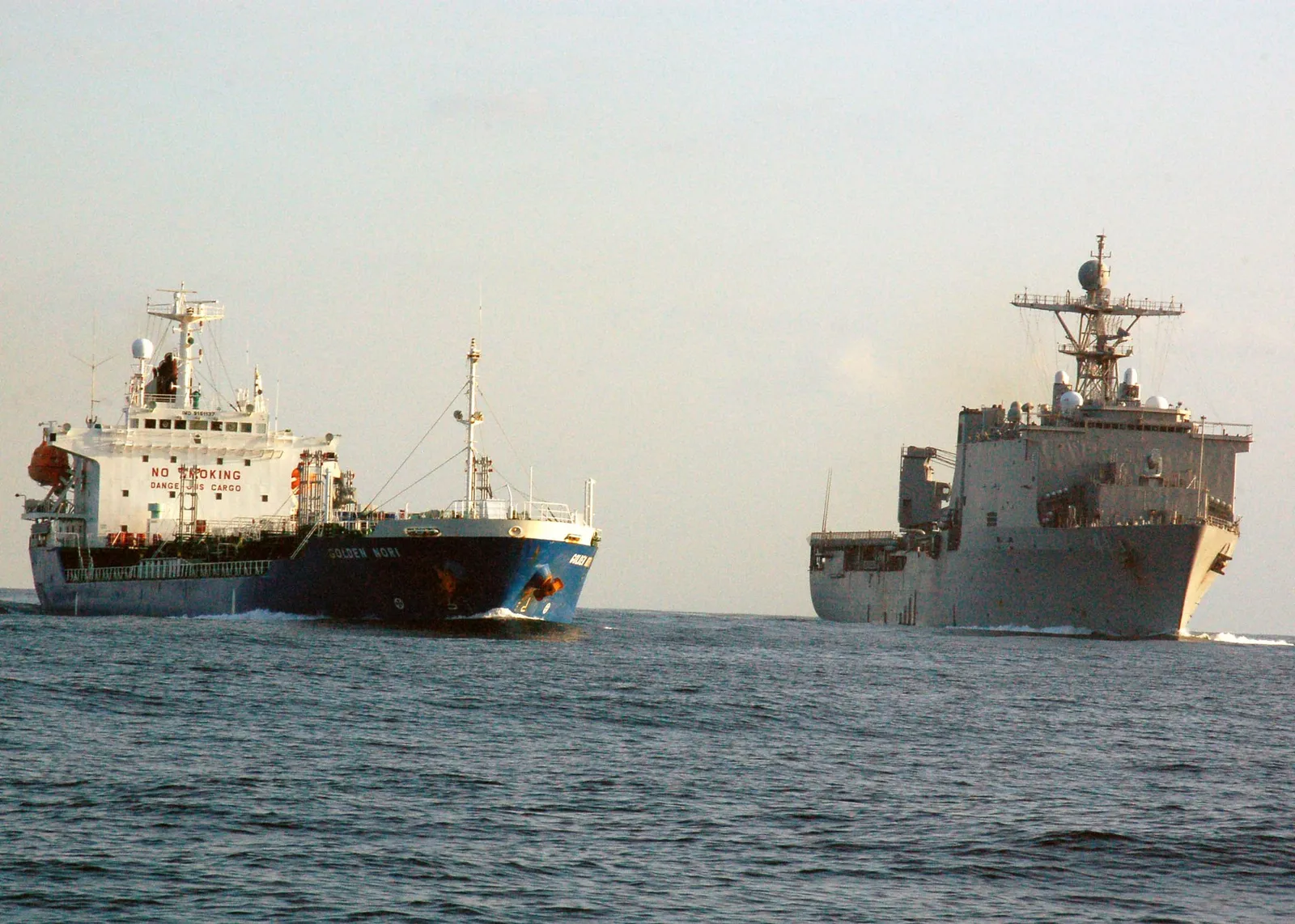 A merchant tanker sails ahead of a grey US Navy ship in the Gulf of Aden.