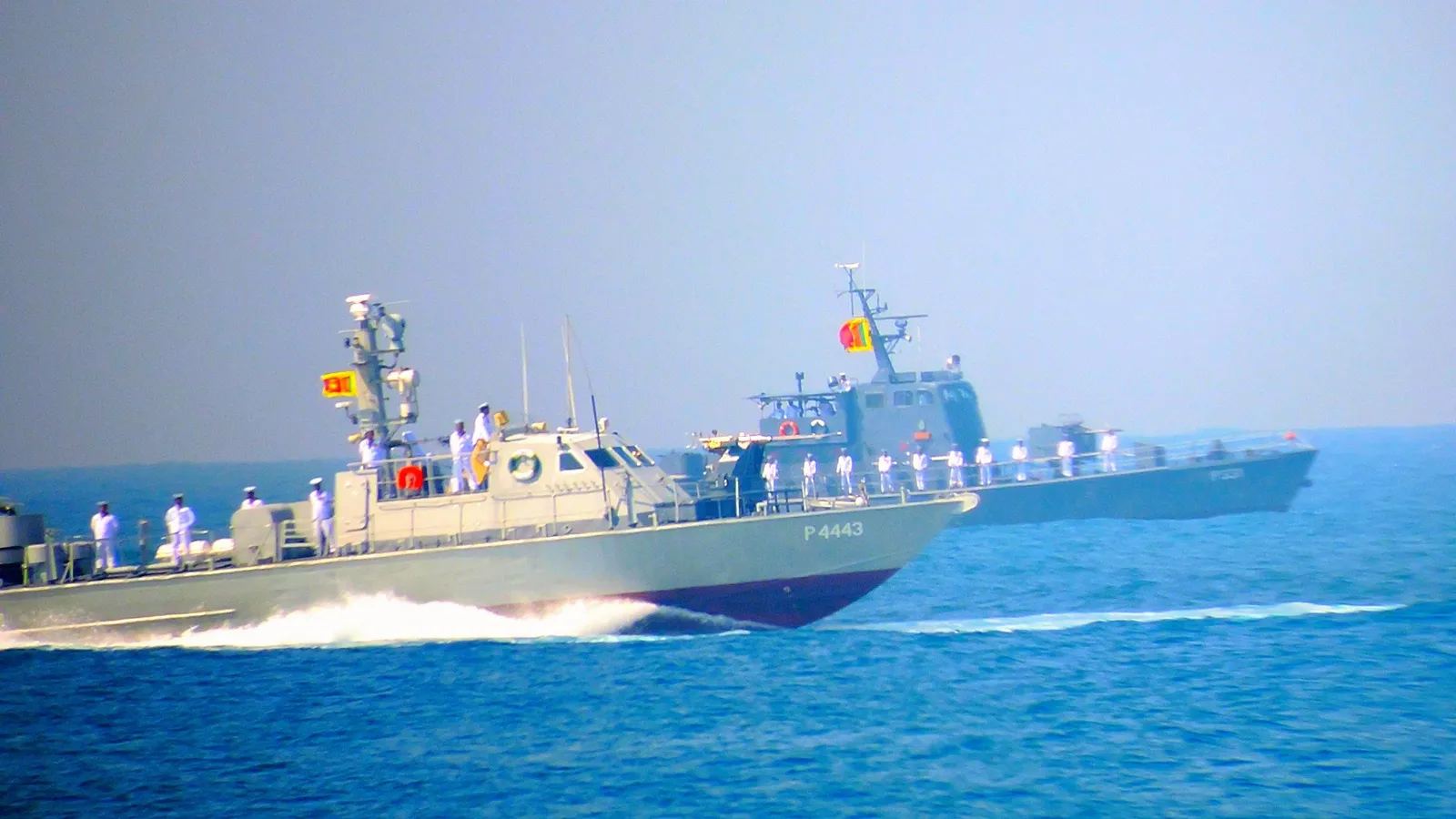 Two grey Sri Lanka Navy patrol boats with sailors in white uniforms on deck, moving fast at sea