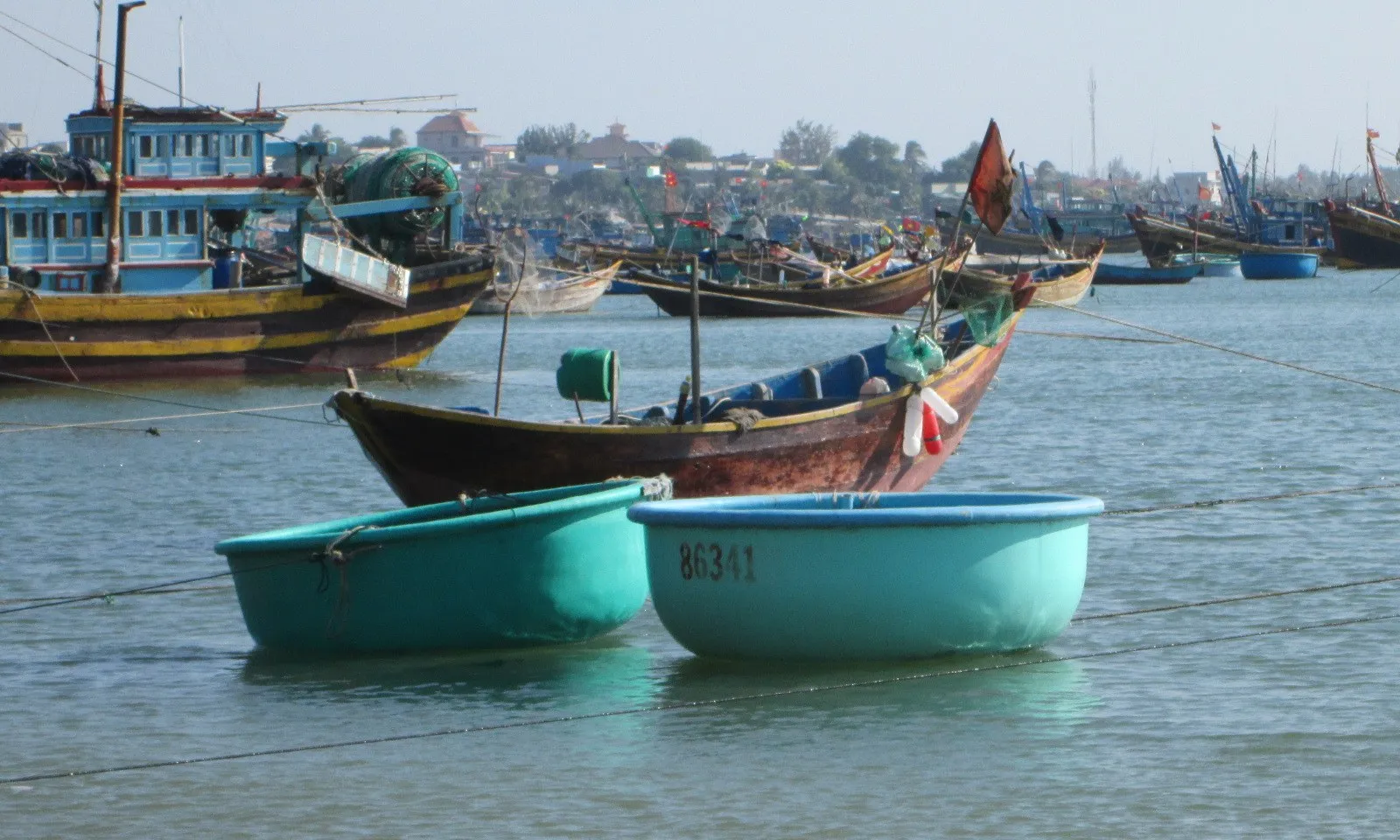 Two round turquoise basket boats float in front of wooden fishing boats in a busy harbour.