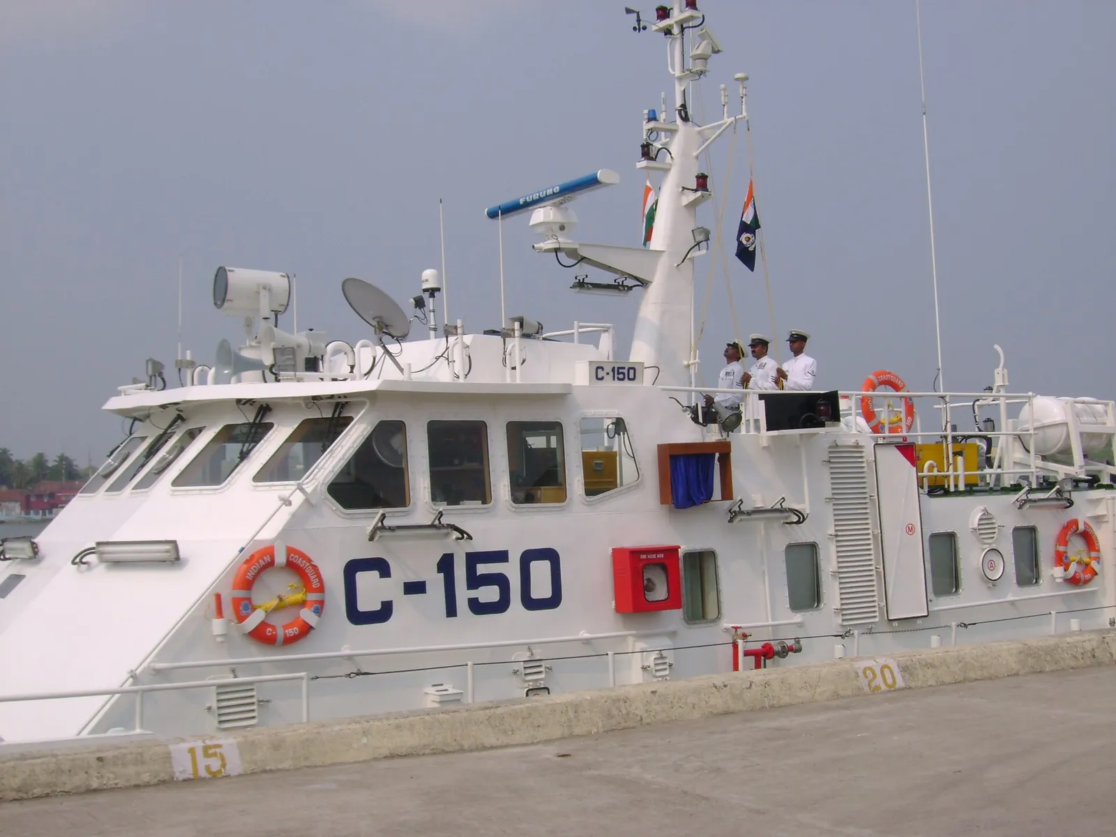 A white Indian Coast Guard patrol boat marked C-150 at a quay, with officers on deck