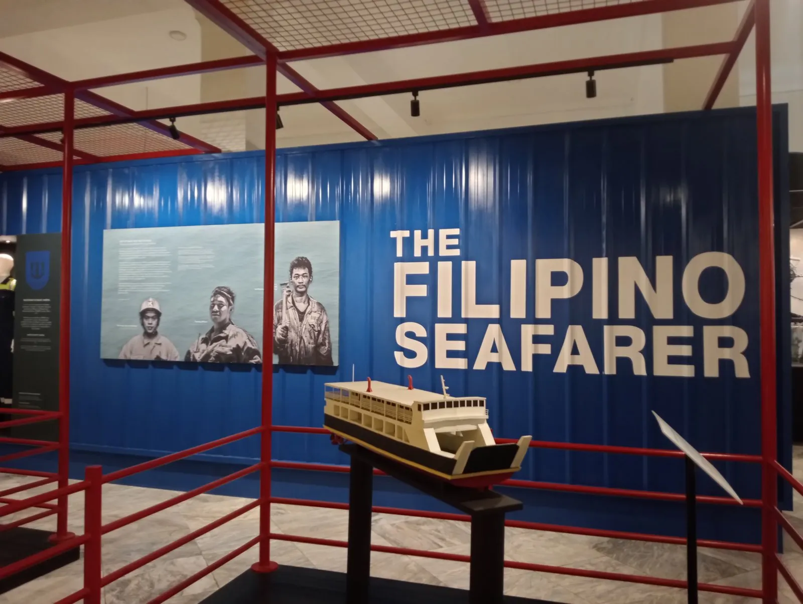 A museum display with a blue wall reading The Filipino Seafarer, an image of three seafarers and a model of a passenger ship on a stand.
