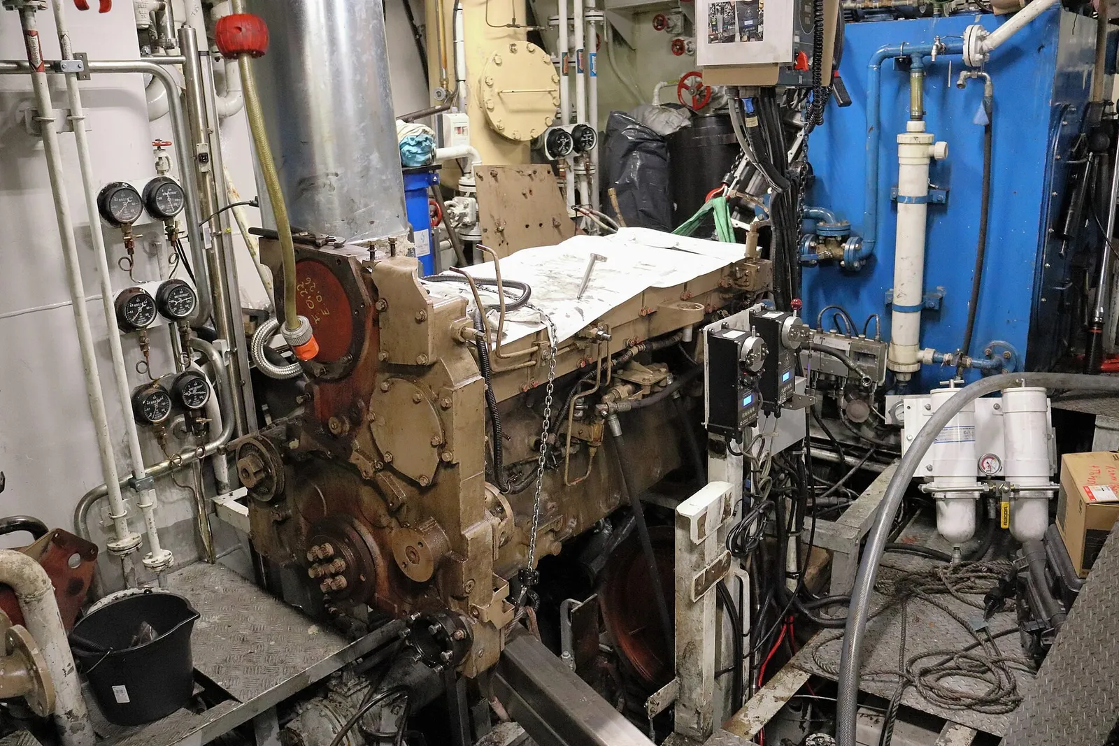 A ship engine room with an engine partly taken apart, pipes, gauges and tools around it.