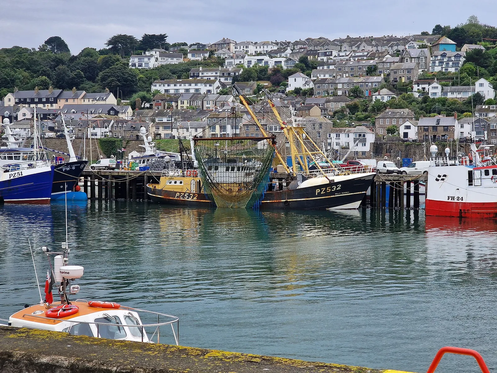 A fishing trawler at a quay in Newlyn harbour, with houses on the hill behind