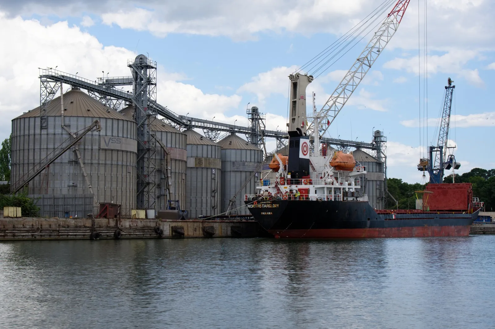 A cargo ship moored beside large silos and cranes in the port of Varna.